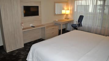 A hotel room with a bed, a desk with a chair, a television, and a window with curtains.