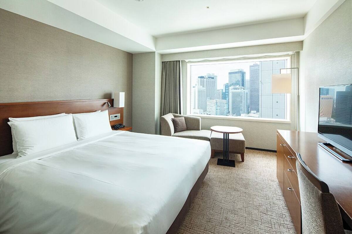 A hotel room with a large bed, a desk, a chair, a small table, and a TV.