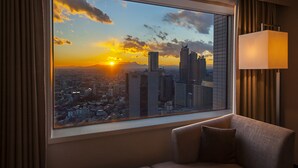 A room with a large window offering a cityscape view at sunset, a sofa, and a lamp. - Century Southern Tower Hotel (Tokyo)