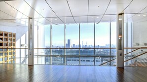 A spacious room with a wooden floor, large windows offering a city view, and a staircase on the right. - Century Southern Tower Hotel (Tokyo)