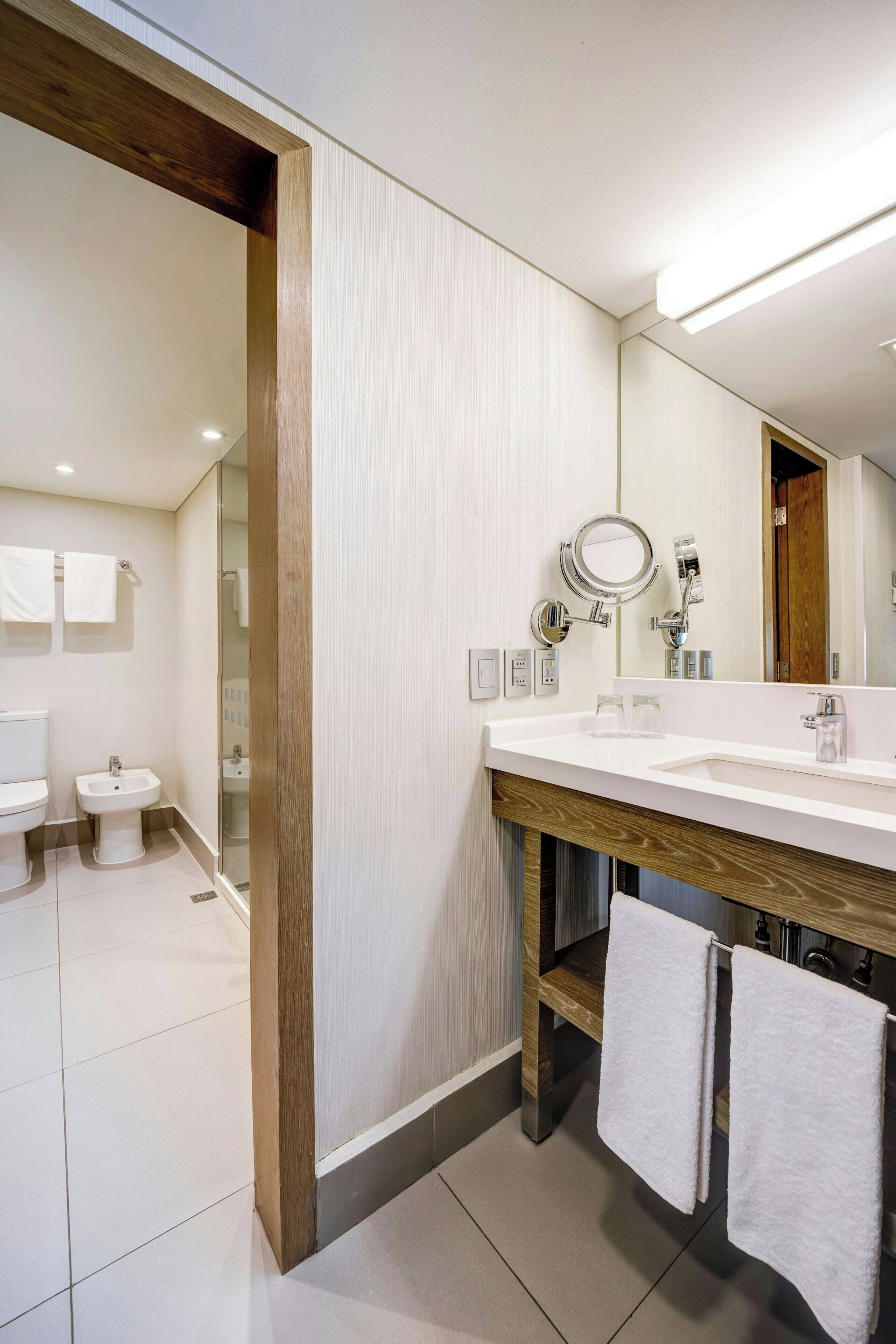 A modern bathroom with a wooden vanity, a large mirror, and a separate sink.