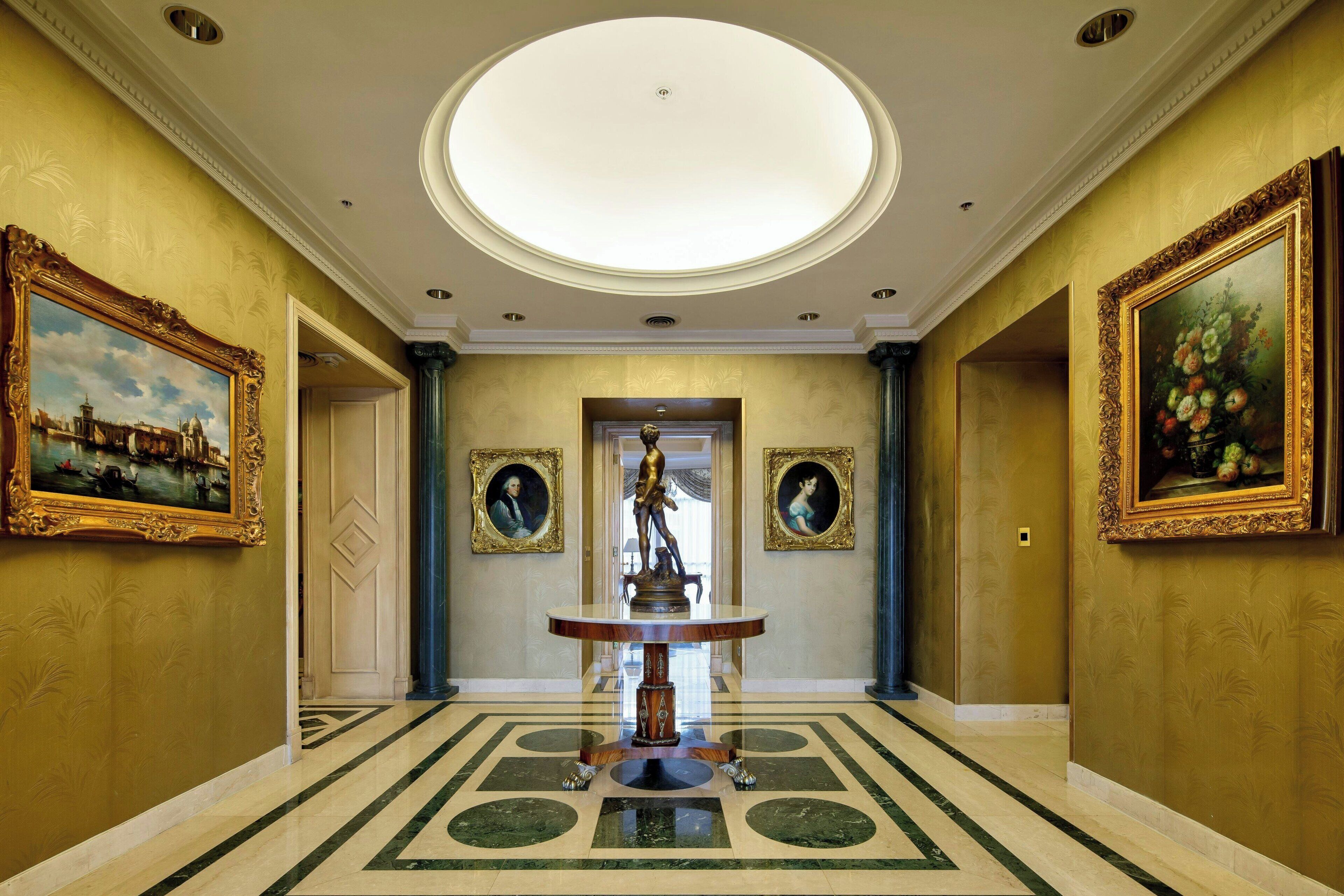 A grand hallway with a marble floor, a central statue, and framed artwork on the walls.