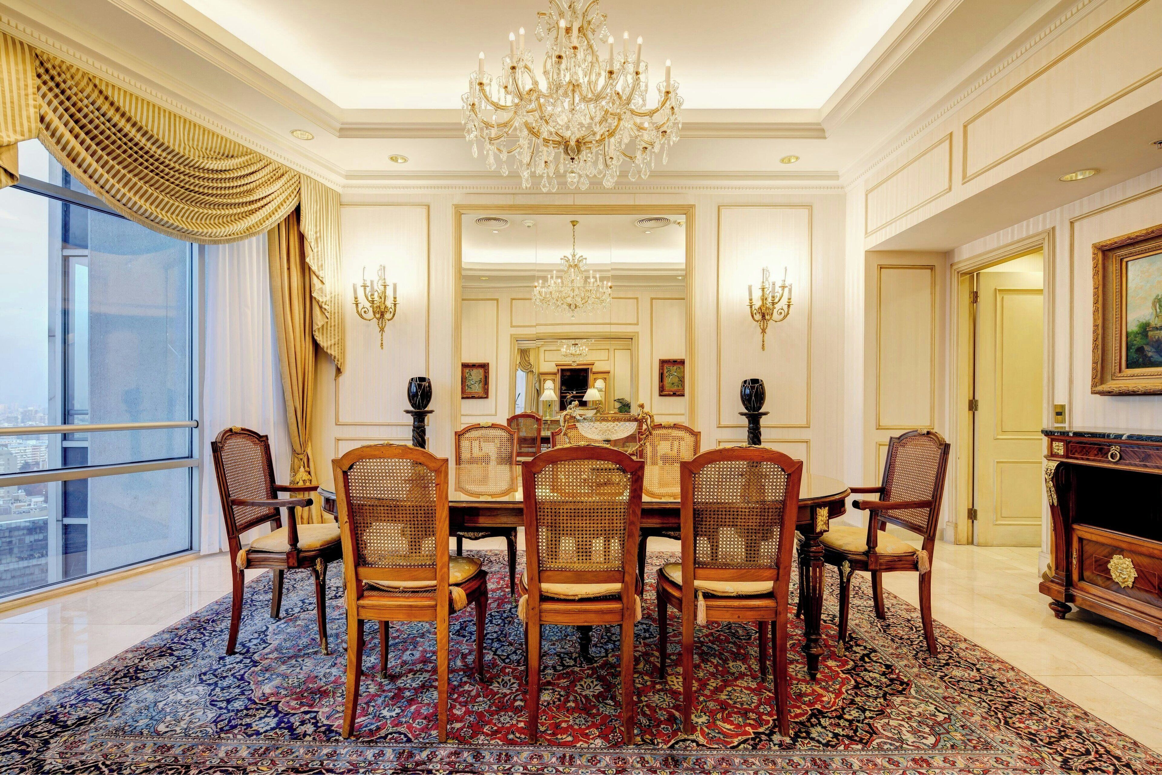 Une salle à manger élégante, agrémentée d’un lustre, de fauteuils richement décorés et d’un grand miroir.