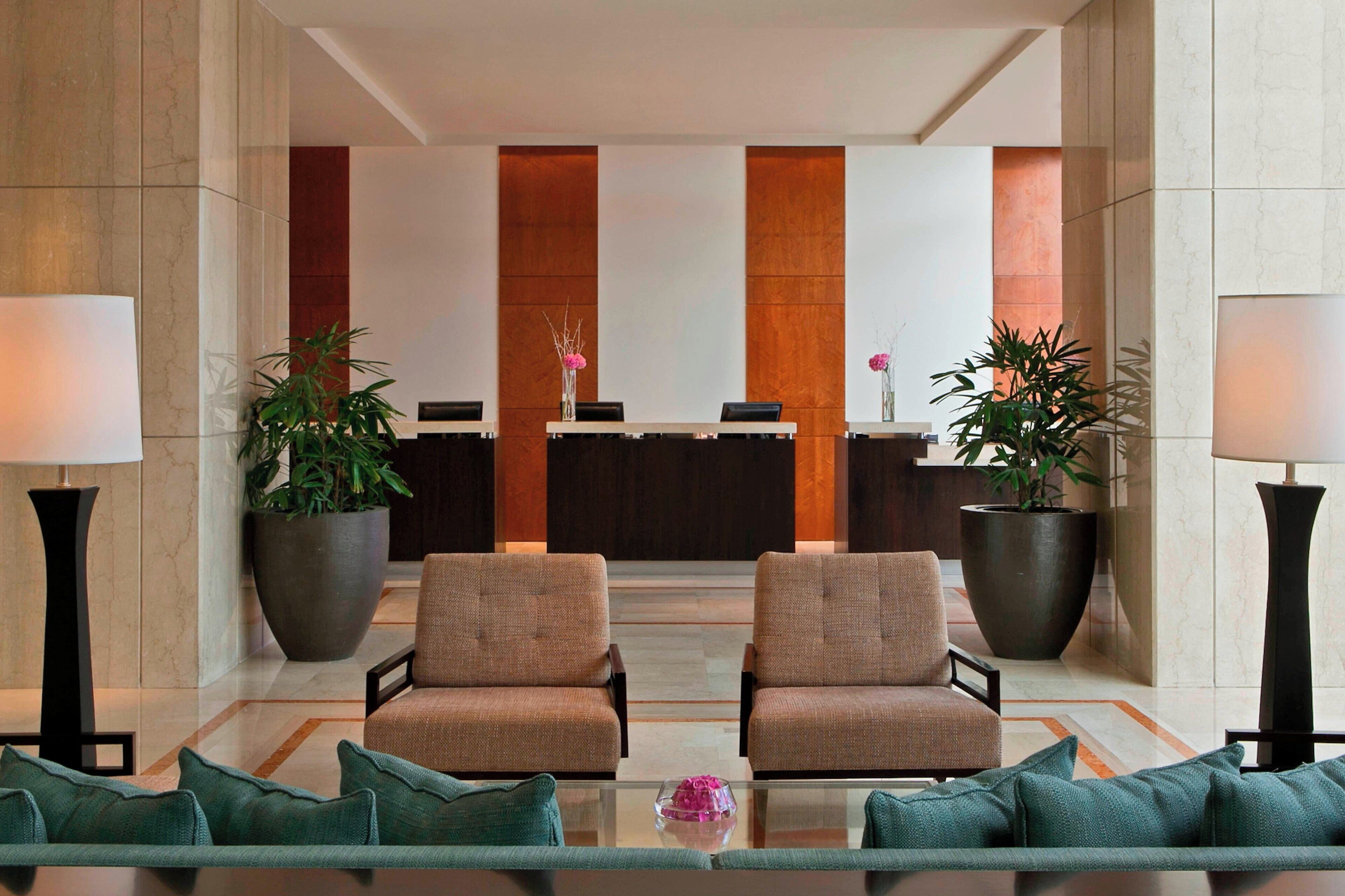 A lobby with two armchairs, a reception desk, and large potted plants.