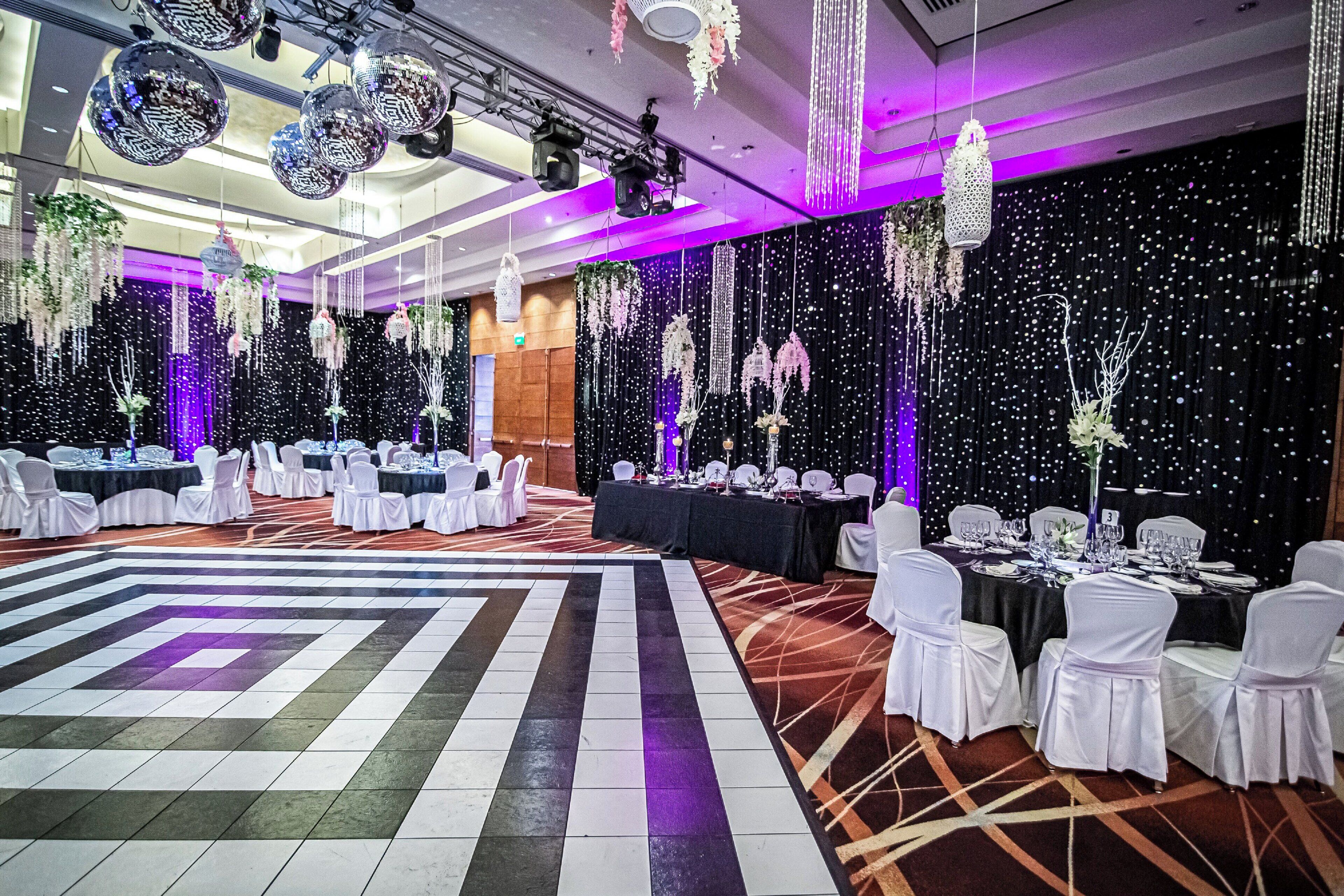 Une salle de bal avec une piste de danse centrale, des tables dressées pour le repas et des décorations suspendues.