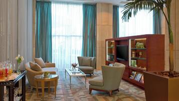 A living room with a sofa, armchairs, a coffee table, a TV stand with books and decorative items, and a large plant.