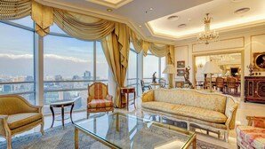 Ein luxuriöses Wohnzimmer mit einem großen Glastisch, eleganten Sofas und Blick auf die Stadt durch raumhohe Fenster.
