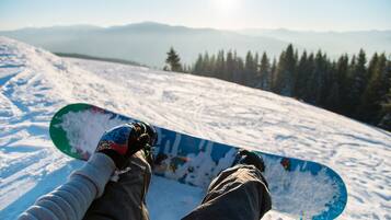 A person sitting on a snow-covered slope with a snowboard, overlooking a forested mountain range.
