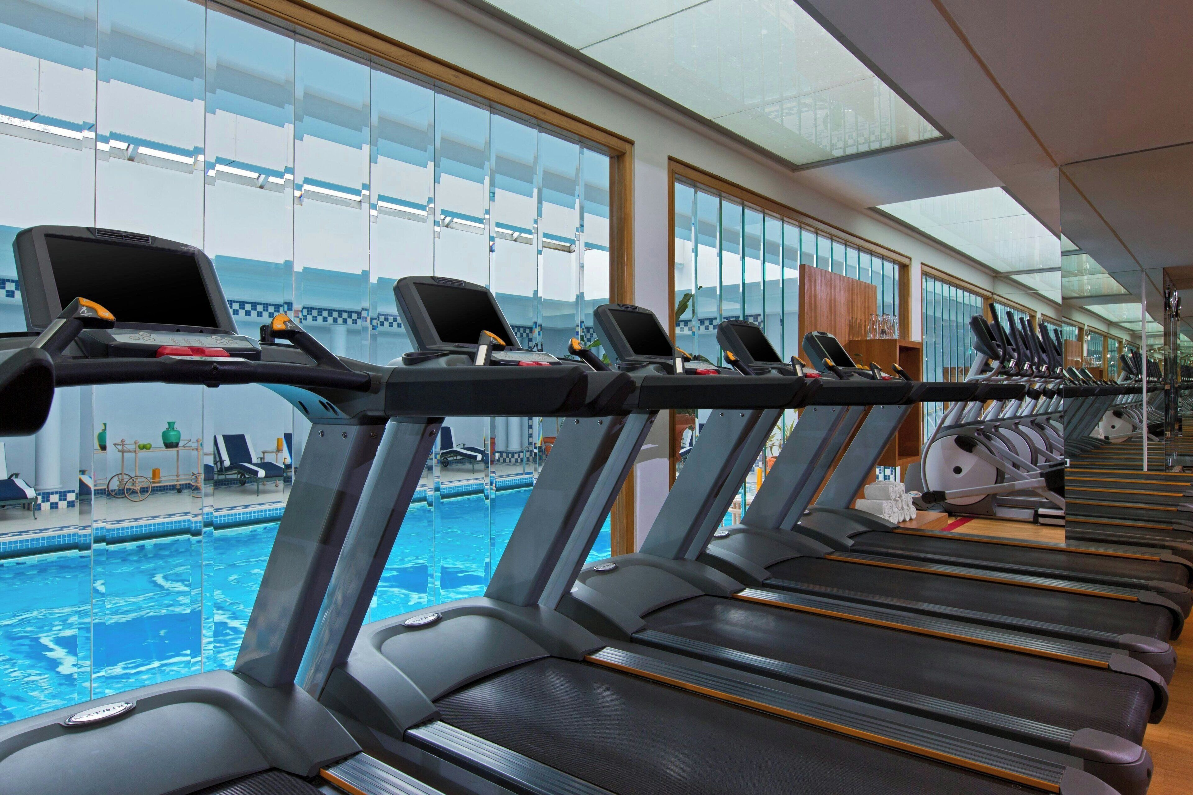 A row of treadmills with a pool visible through the glass walls.