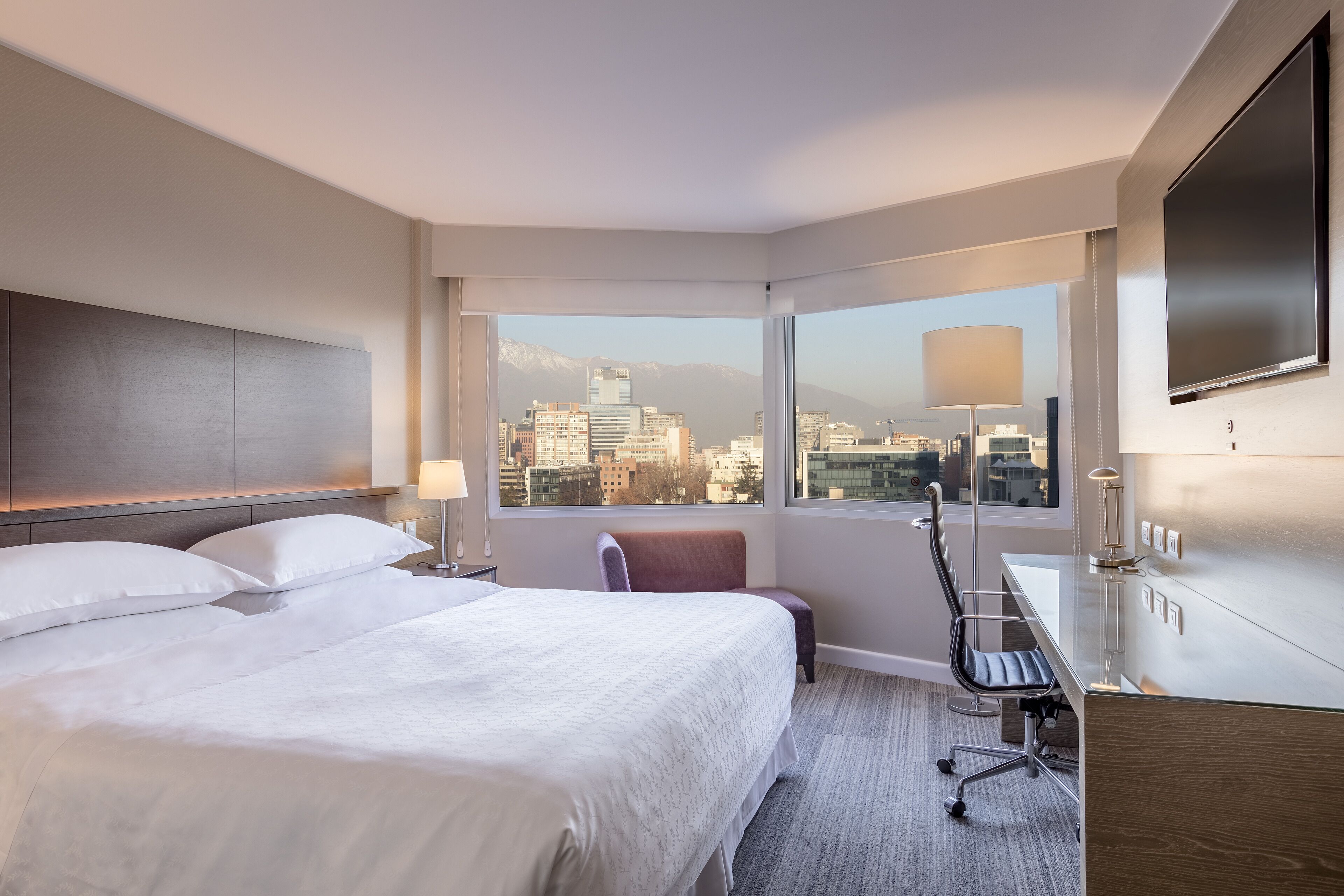 Une chambre d’hôtel avec un grand lit, un bureau, une chaise et un téléviseur.