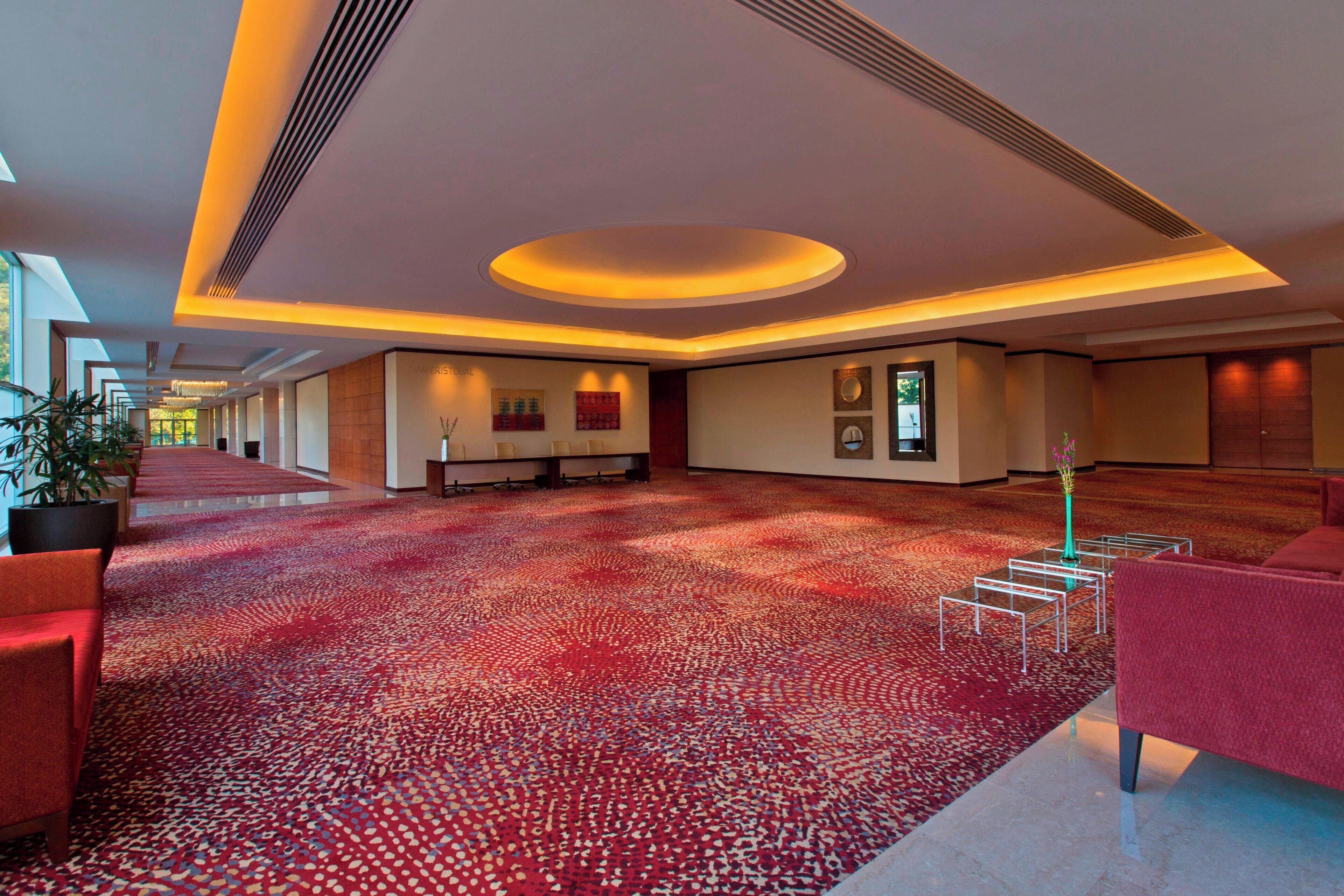 Un amplio vestíbulo de hotel con alfombra de estampado rojo, mobiliario moderno y una zona de estar amplia.
