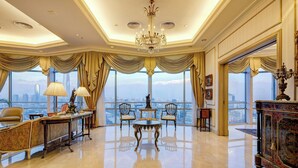 Ein luxuriöses Zimmer mit einem großen Chandelier, stilvollem Mobiliar und Blick auf die Stadt durch große Fenster.
