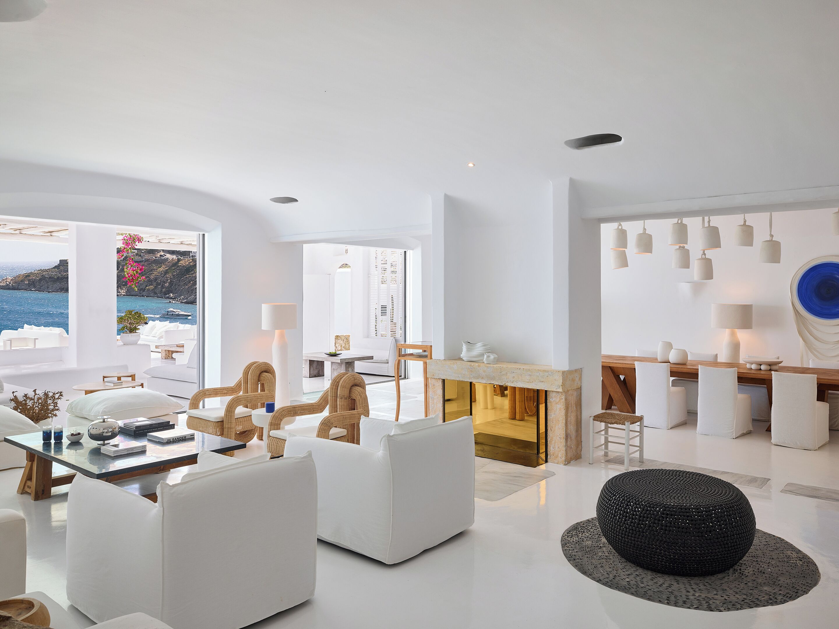 A modern living room with white furniture, a fireplace, and a view of the sea.