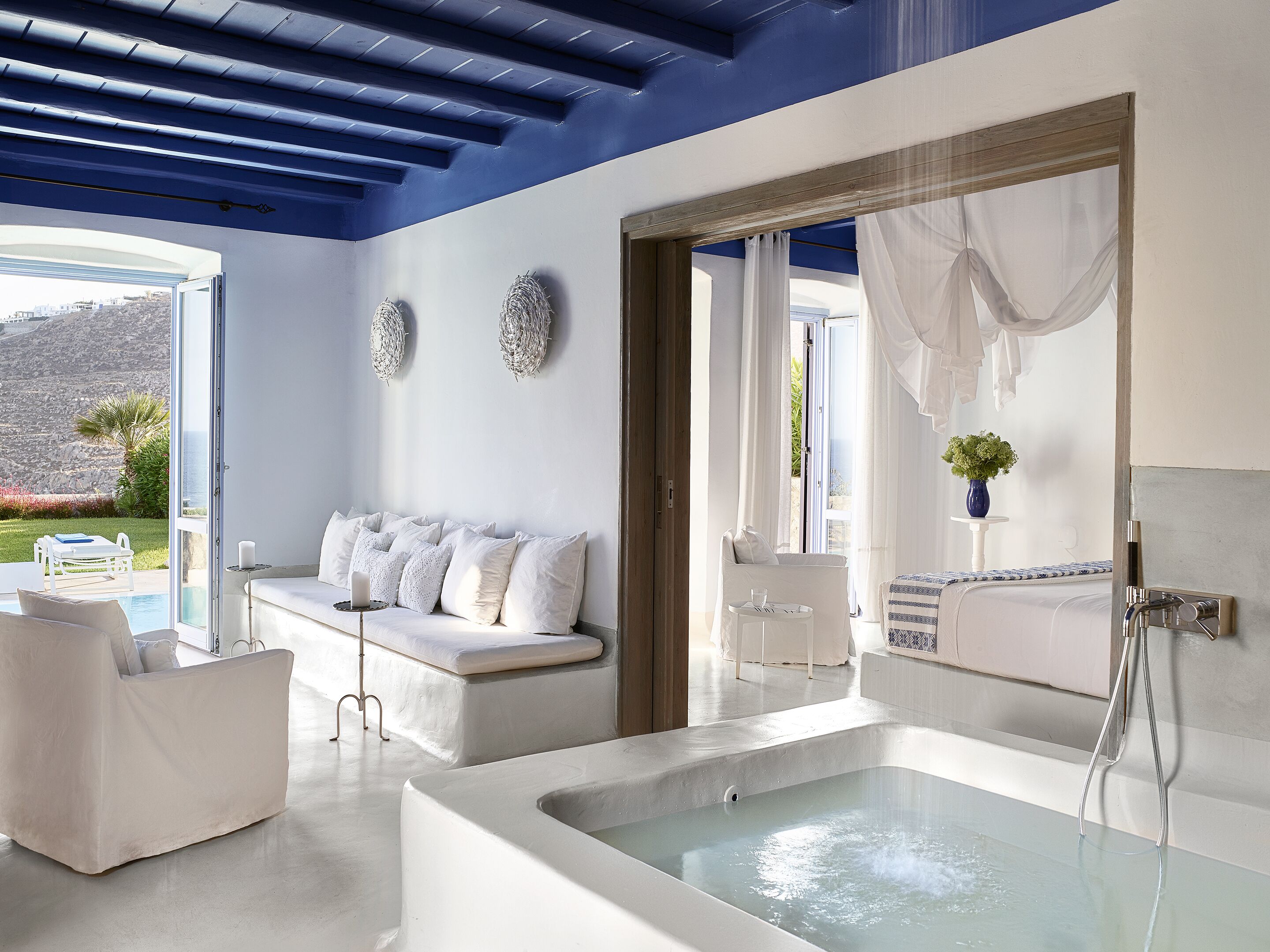 A modern bathroom with a bathtub, a white sofa, and a view of the outdoors.