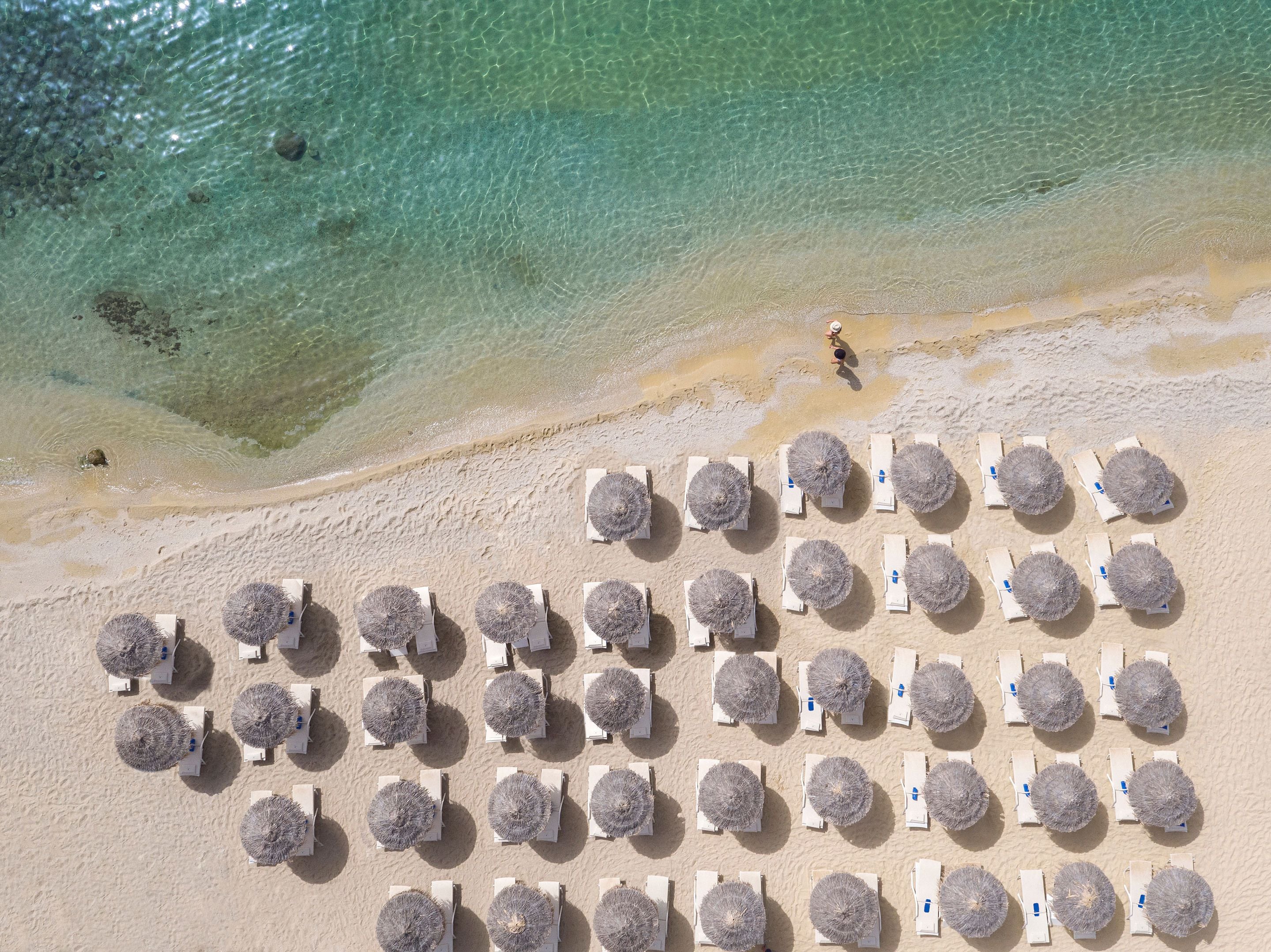 An aerial view of a beach with rows of sun loungers and thatched umbrellas.