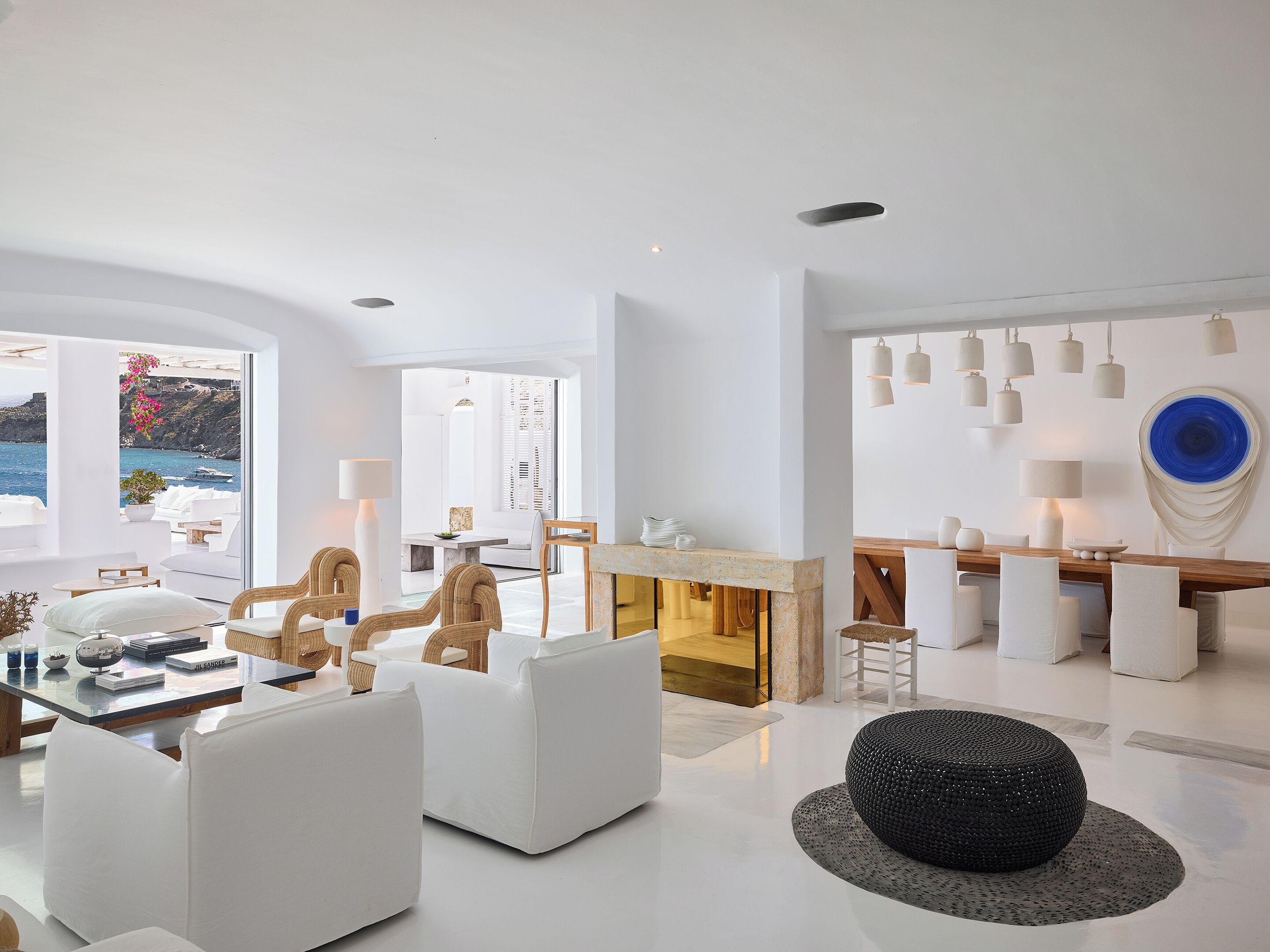 Uma sala de estar moderna com móveis brancos, uma área de jantar com mesa de madeira e vista para o mar.
