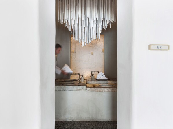 A modern bathroom with a stone sink, a wooden countertop, and a hanging light fixture. - Mykonos Blu, A Resort to Live (Mykonos)