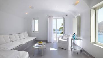 Una habitación moderna y minimalista con un sofá blanco, una mesita redonda y una silla. Un ventanal grande ofrece vistas al mar.