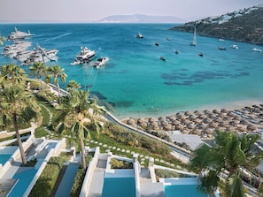 A resort with multiple swimming pools, a beach area with umbrellas, and boats in the water. - Mykonos Blu, A Resort to Live (Mykonos)