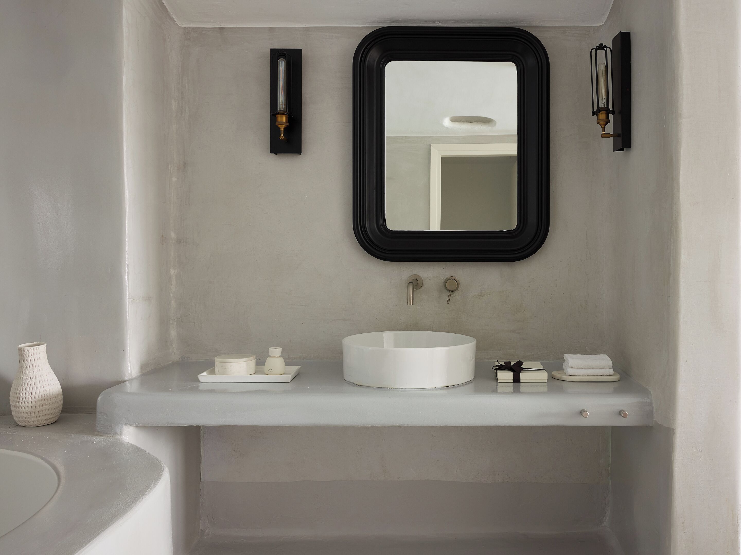 Ein Badezimmer mit einem weißen Waschbecken, einem runden Spiegel und zwei Wandleuchten.
