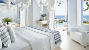 A bedroom with a bed, a desk, and a view of the ocean.