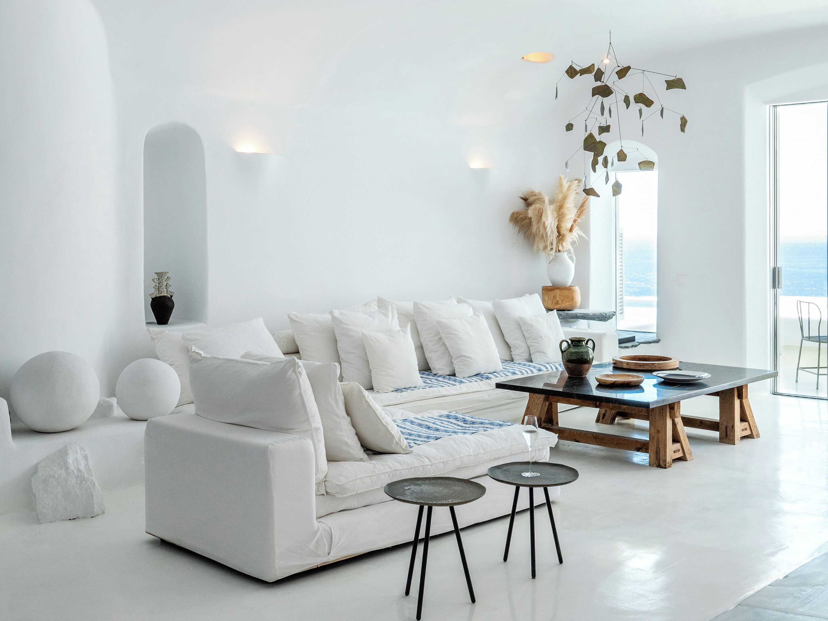 A minimalist living room with a white sofa, two small tables, and a view of the sea through a large window.