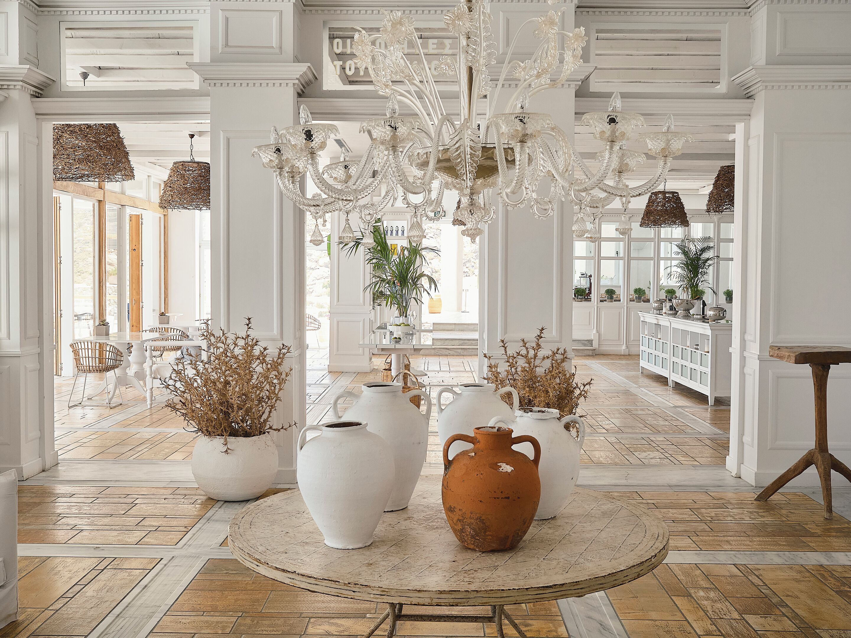 A spacious room with a large white chandelier, multiple vases, and a round table with a rustic finish.