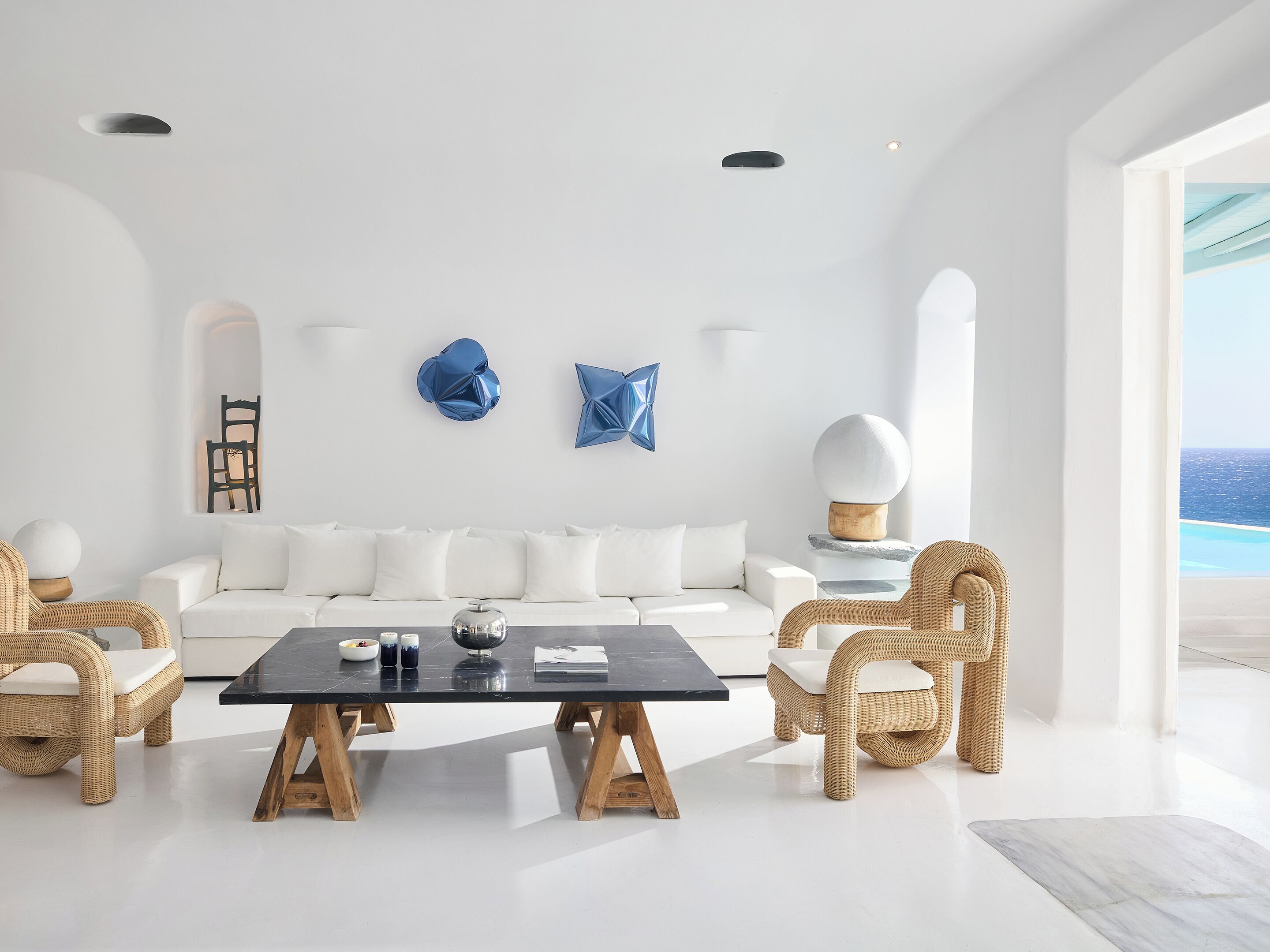 A modern living room with a white sofa, two wicker chairs, a black coffee table, and abstract wall art.