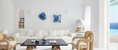 A modern living room with a white sofa, two wicker chairs, a black coffee table, and abstract wall art.