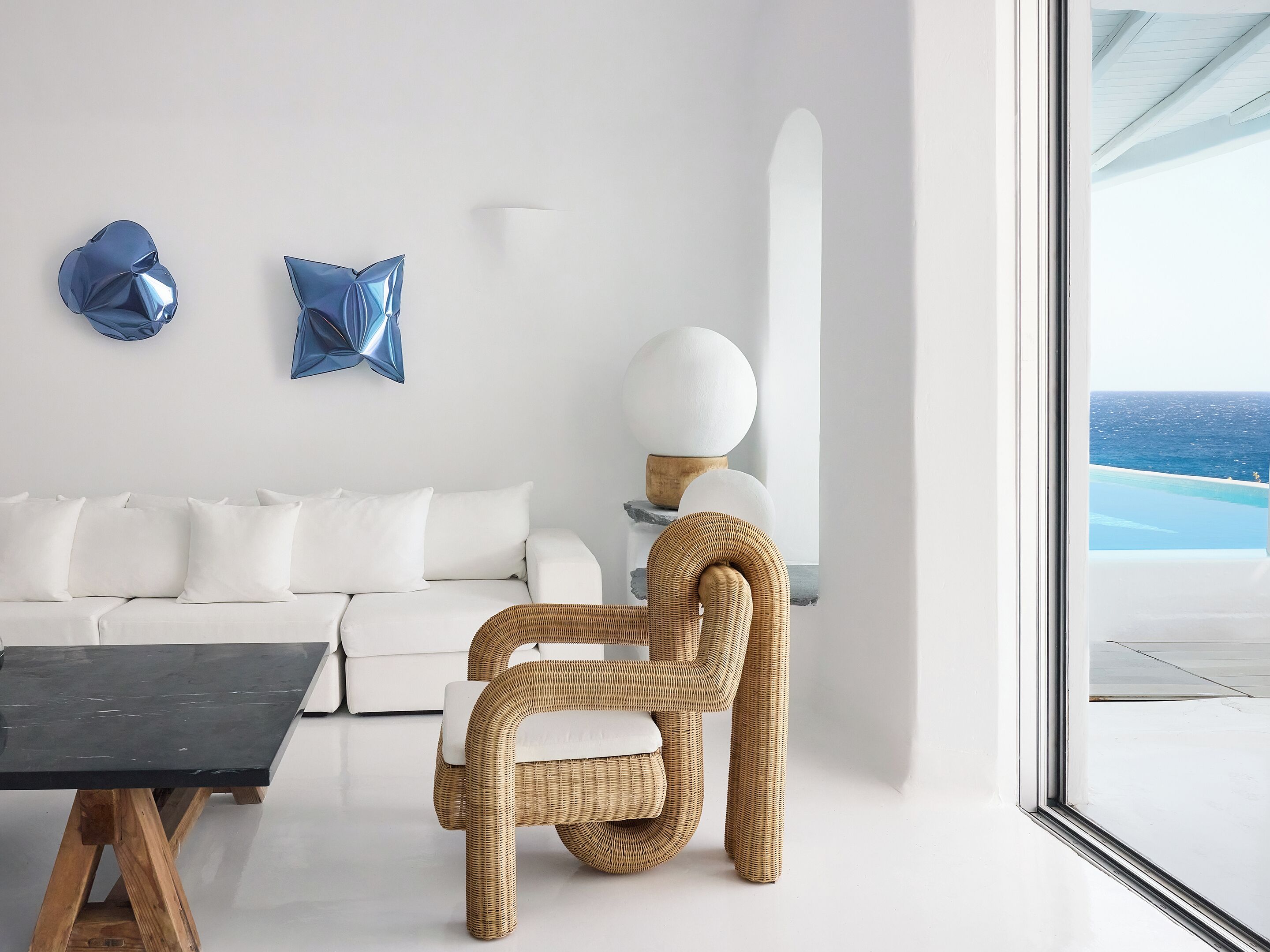 A modern living room with a white sofa, a wicker chair, and a black table.