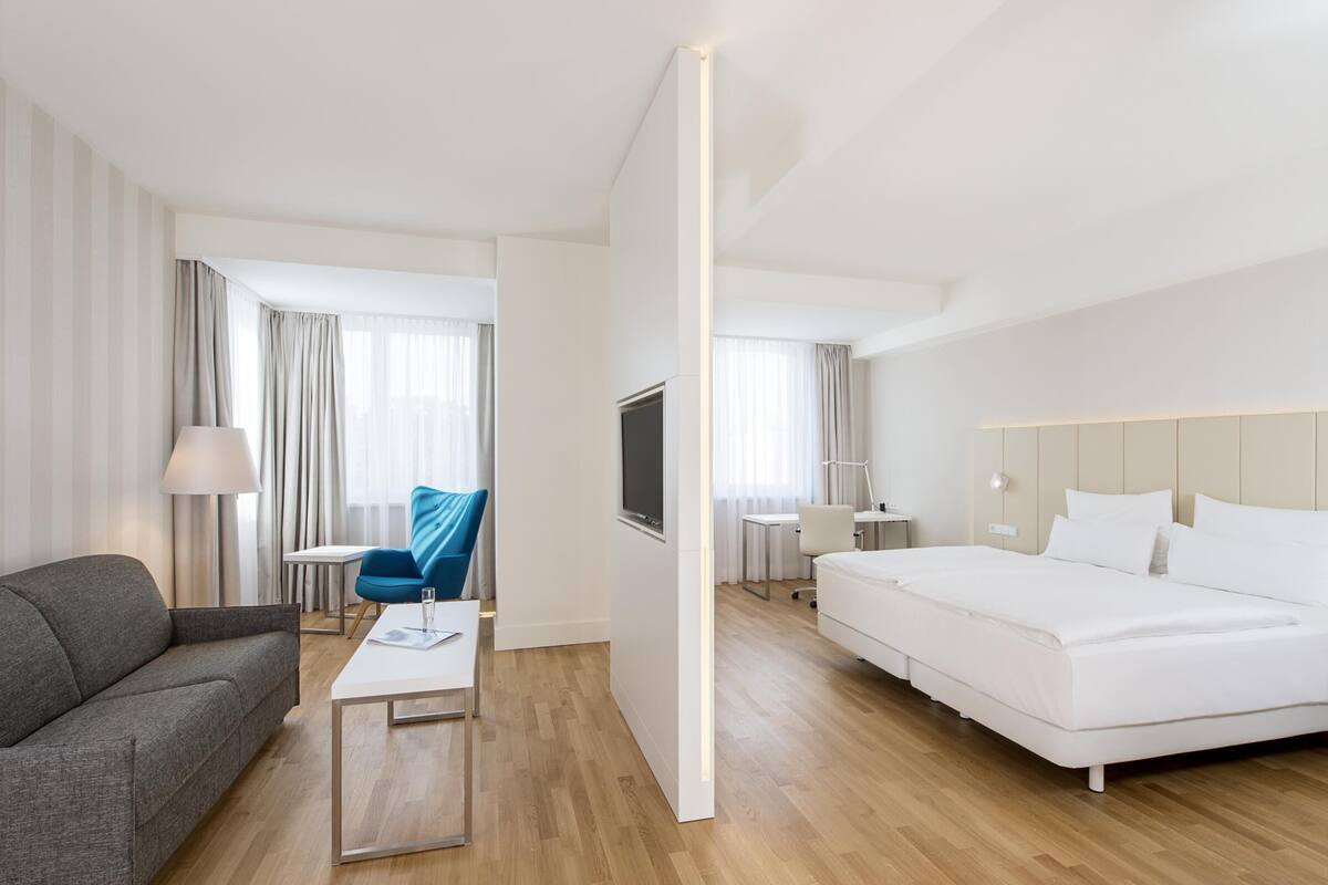 A modern hotel room with a large bed, a sofa, a desk, and a TV.