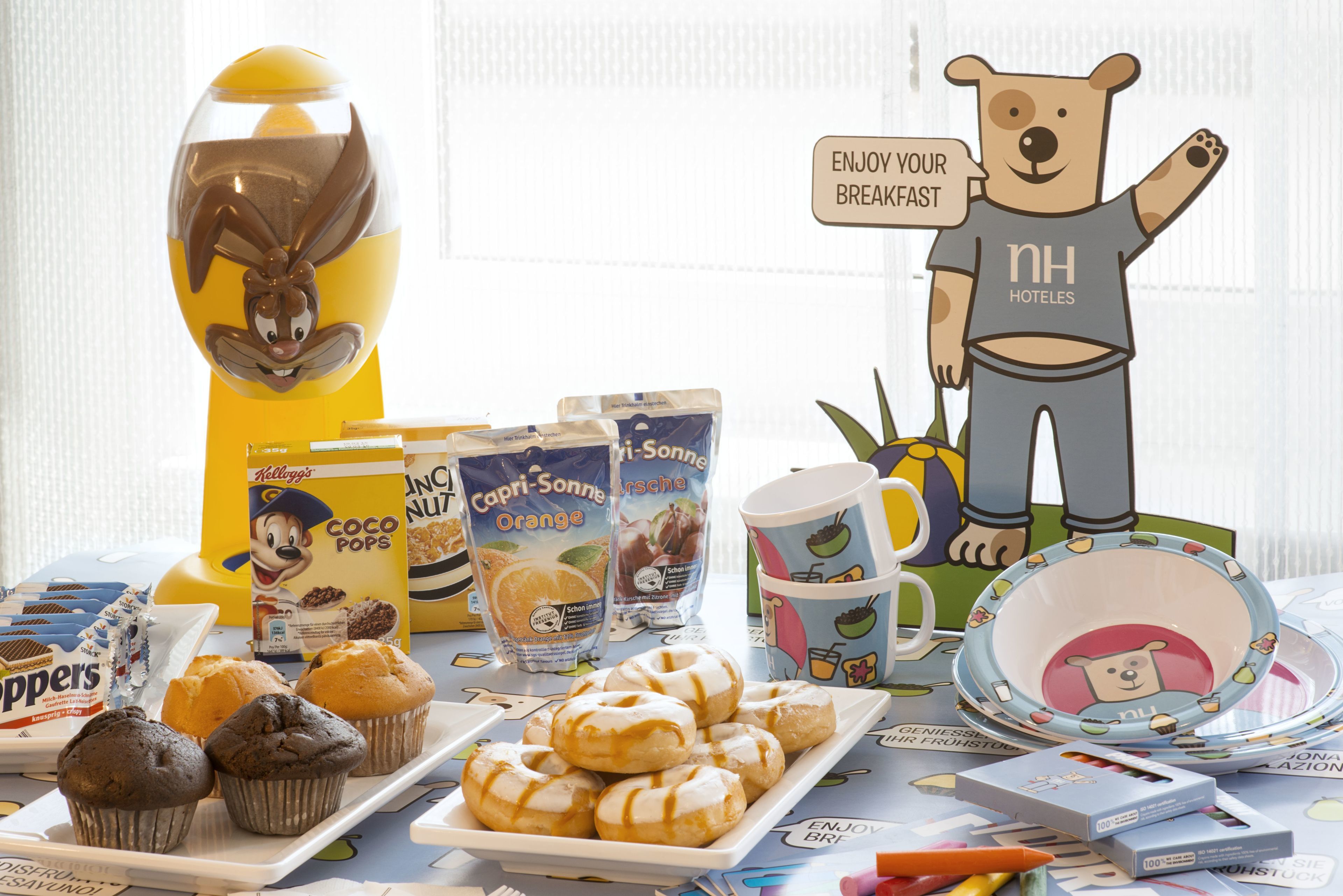 Una mesa de desayuno con pasteles, café y una figura de un oso de caricatura.