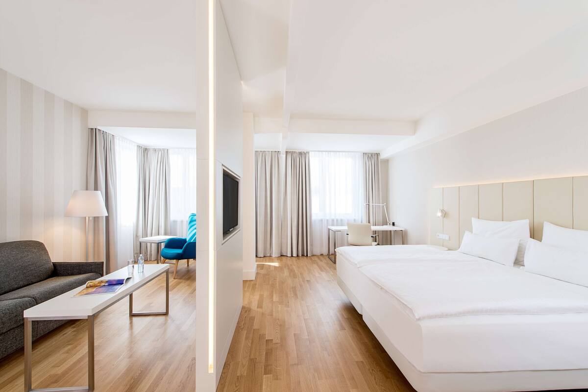 A modern hotel room with a large bed, a sofa, a small table, and a TV.