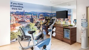 A fitness room with two exercise bikes, a water dispenser, and a large poster of a cityscape. - NH Collection Wien Zentrum (Vienna)