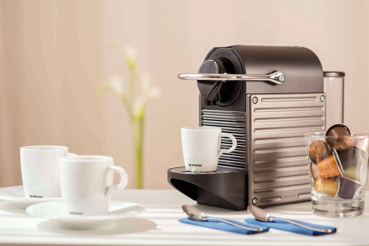 A Nespresso coffee machine with a cup and a glass of coffee on a table.