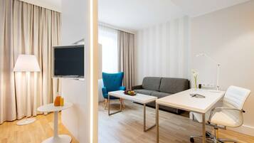 Una habitación de hotel moderna con una televisión de pantalla plana, un sofá, una mesa de comedor y una mesita auxiliar.
