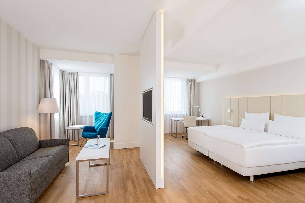 A hotel room with a bed, a sofa, a desk, and a TV.
