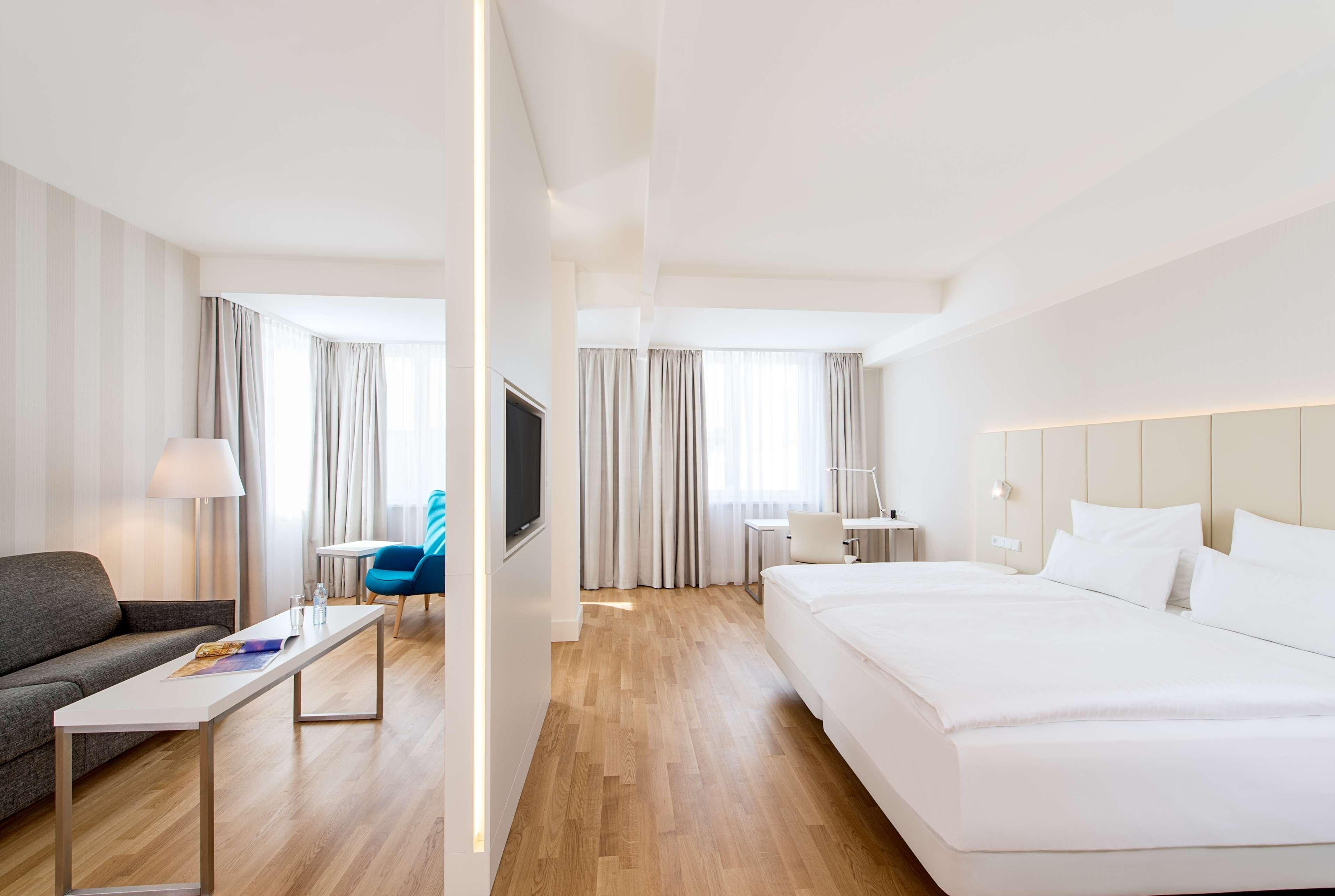 A hotel room with a bed, a sofa, a desk, a chair, and a TV.