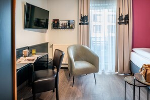 Una habitación de hotel con escritorio, silla, cama y ventana con cortinas.