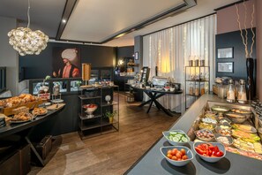 Moderni aamiaisbuffet, jossa on monipuolinen valikoima ruokia, kahvilaitteisto ja koristeellinen taulu.