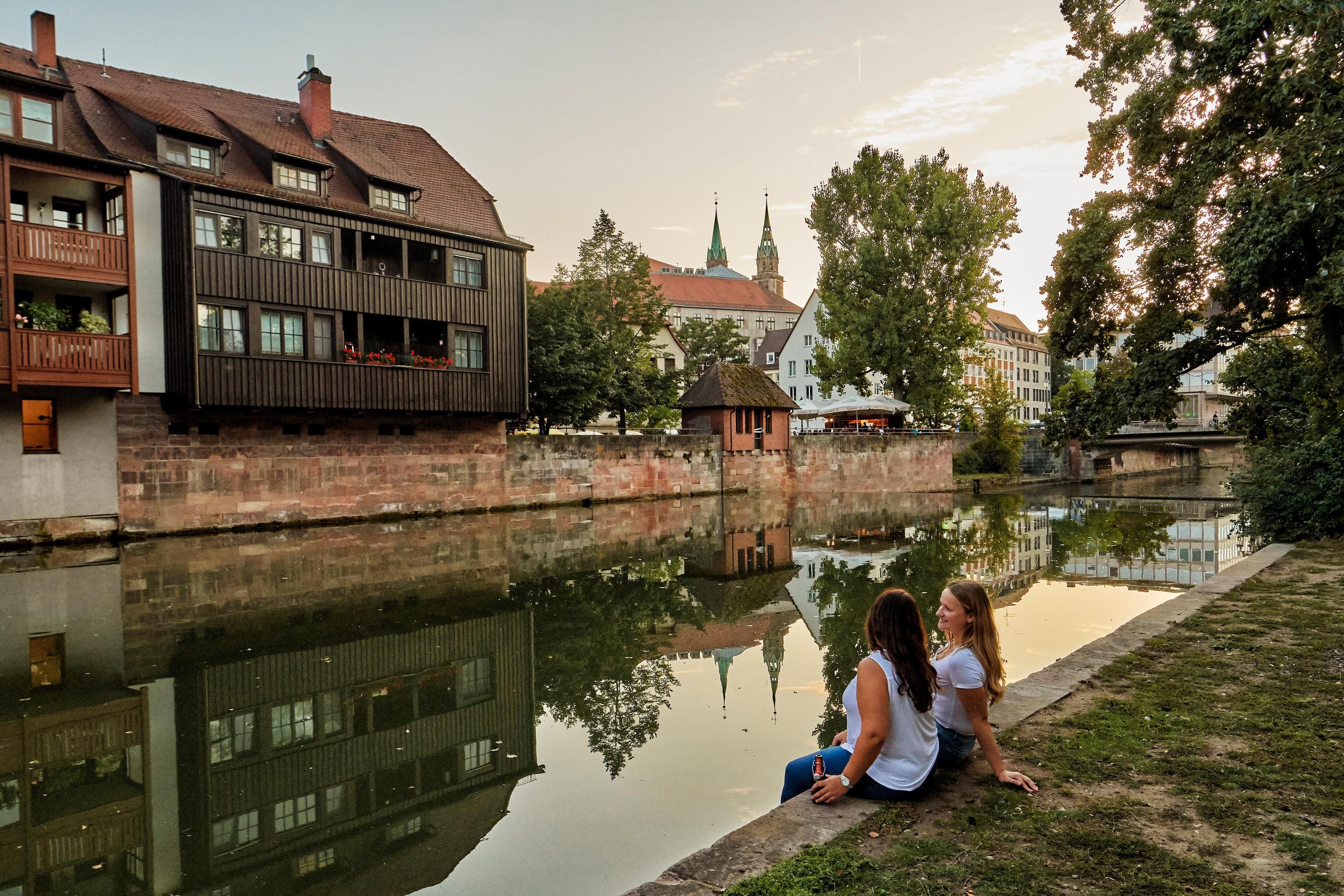 A riverside view with buildings, a bridge, and a reflection in the water.