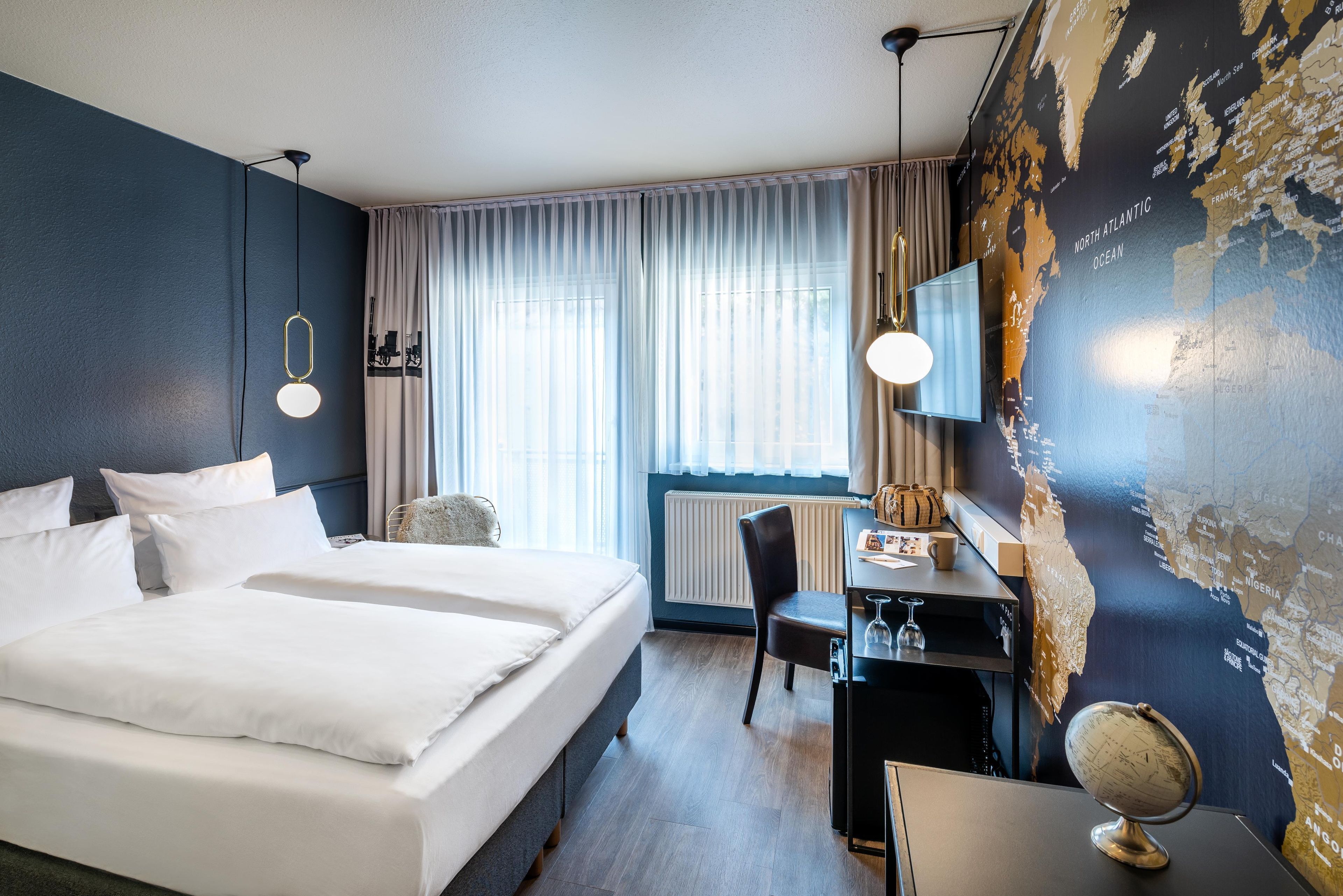 A hotel room with a large bed, a desk, a chair, a globe, and a map on the wall.