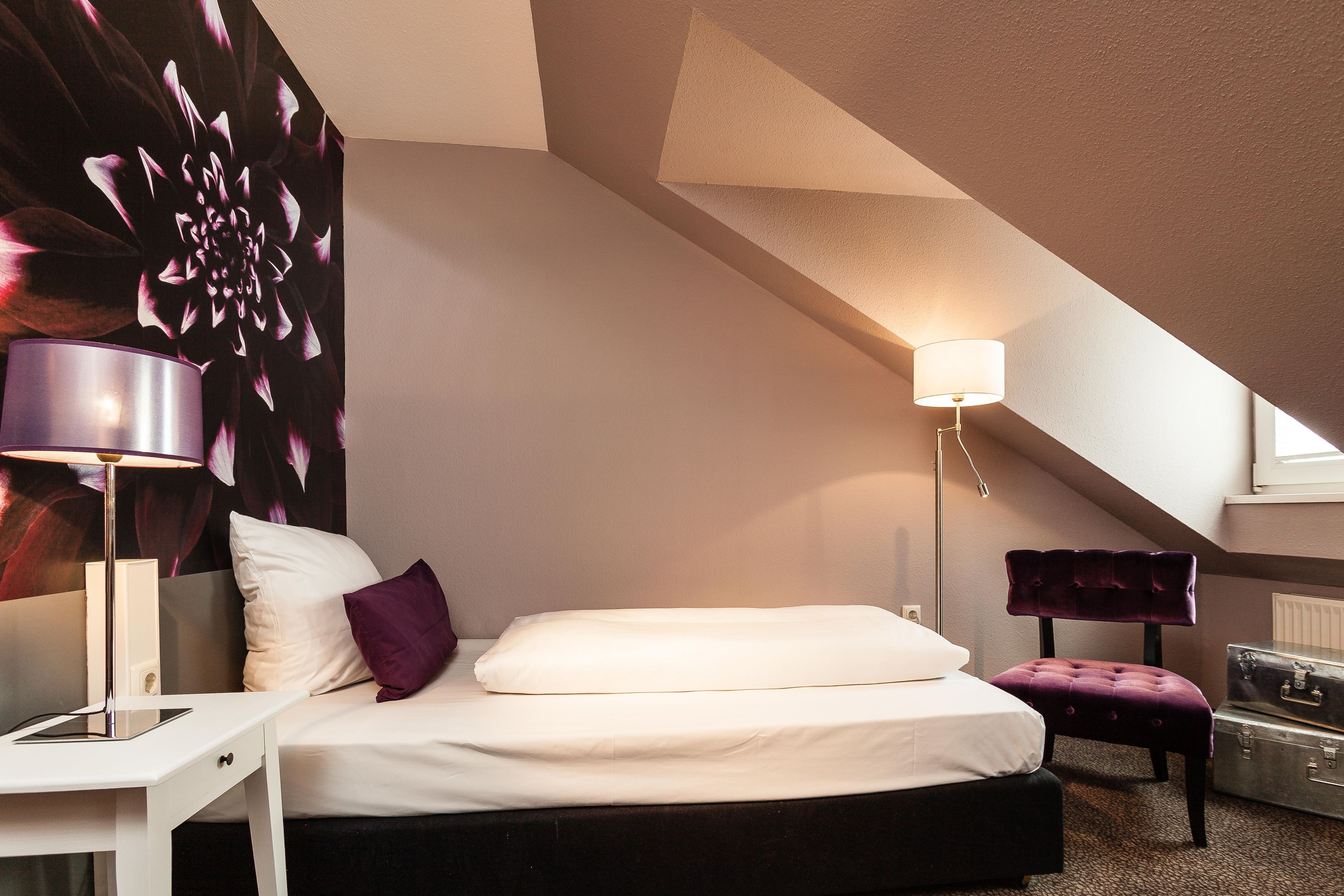 A bedroom with a bed, a desk, a lamp, a chair, and a radiator.