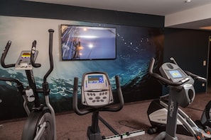 Un espacio de ejercicios con bicicletas estáticas y una pantalla de televisión que muestra una imagen panorámica.