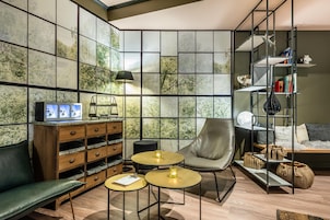 Una sala de estar moderna con un sofá modular, un sillón de cuero, dos mesitas redondas, una estantería y una pared con un diseño de azulejos inspirado en la naturaleza.