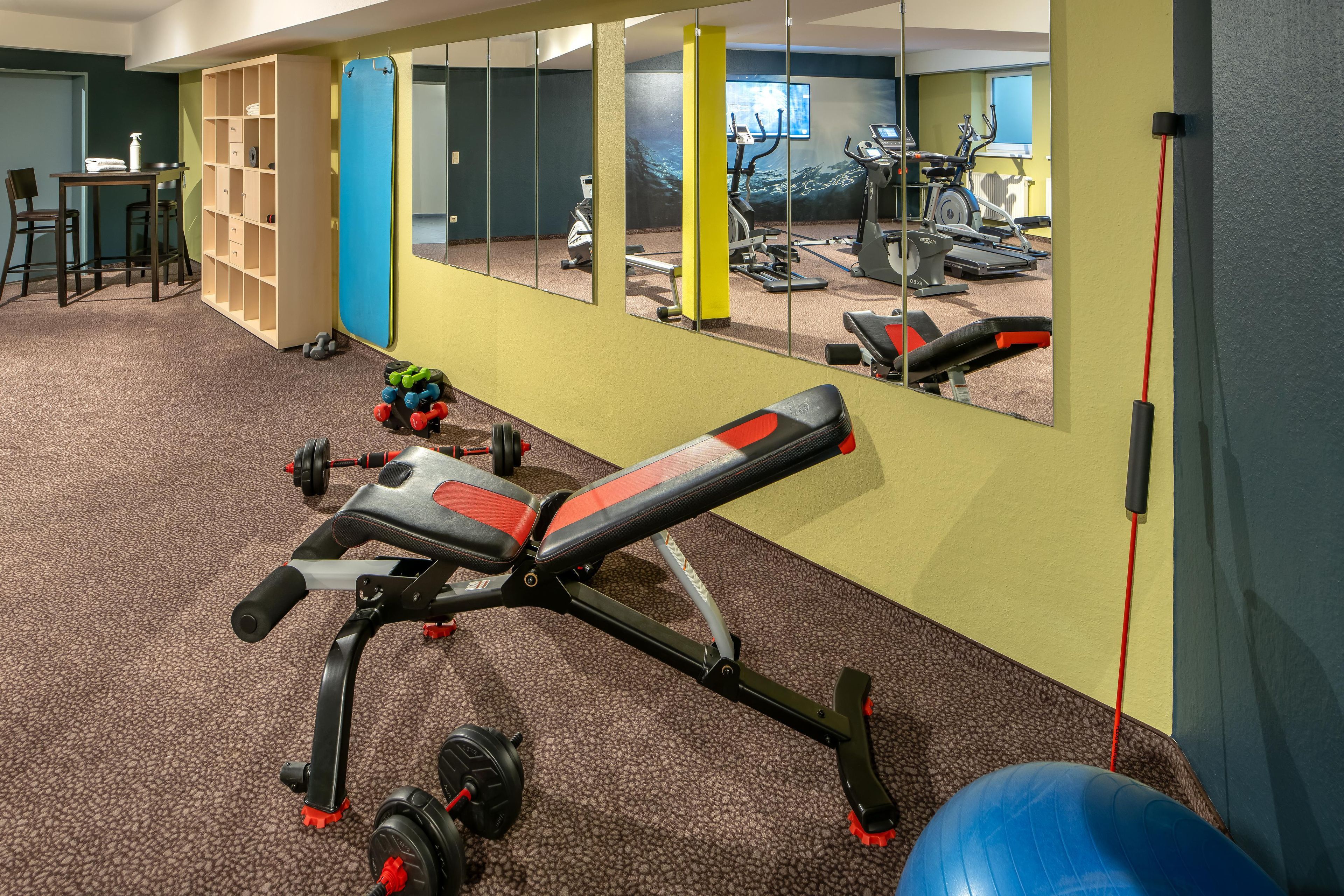 Un gimnasio con equipamiento de ejercicio, un espejo y suelo alfombrado.