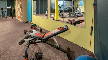 Un gimnasio con equipamiento de ejercicio, un espejo y suelo alfombrado.