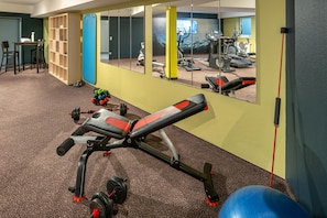 Un gimnasio con equipamiento de ejercicio, un espejo y suelo alfombrado.