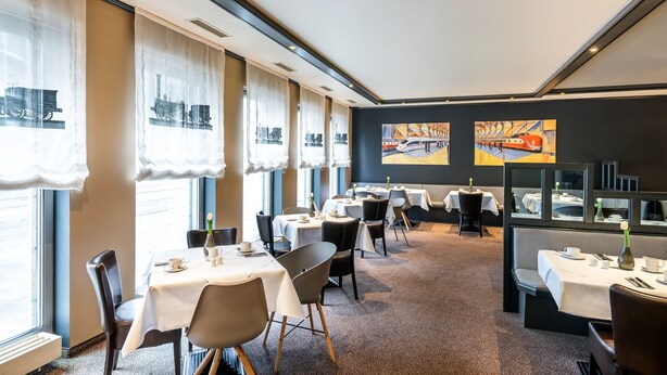 A hotel dining area with tables set for service, large windows with curtains, and artwork on the walls. - Best Western Hotel Nuernberg Am Hauptbahnhof (Nuremberg)