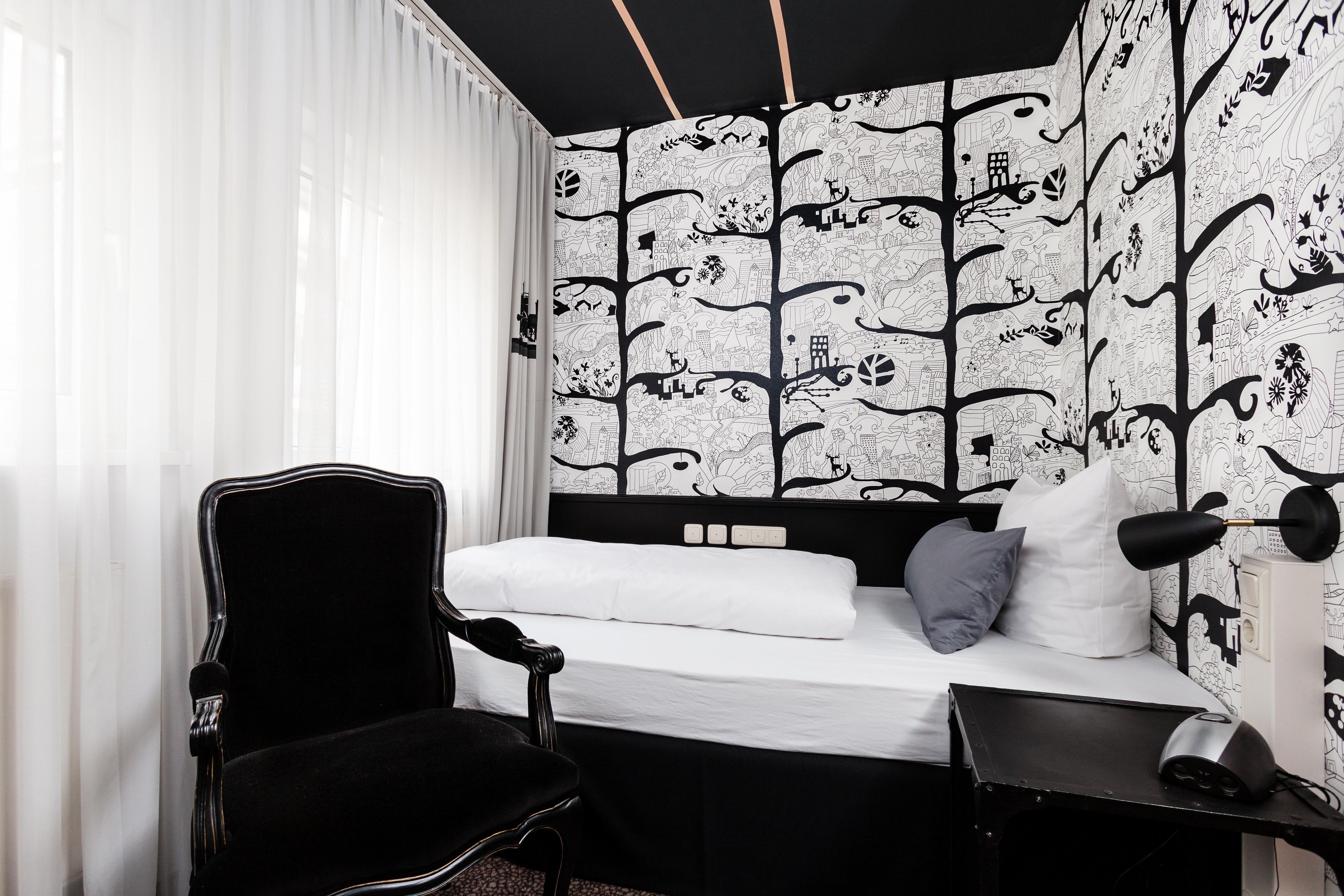 A bedroom with a bed, a chair, a desk, and a wall with a black and white pattern.